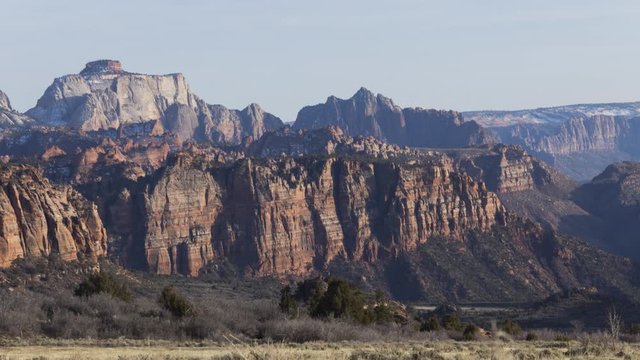 A long-lens timelapse of red cliffs in Zion National Park lighting up with stunning golden light as the sun sets.