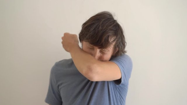 A young man sneezes properly. He sneezes into his elbow