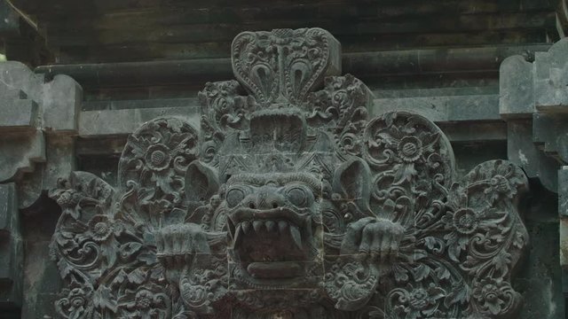 Beautiful sandstone carving of a demon head in a hindu temple in Bali, Indonesia. The eyes, teeth and fangs bared surrounded by carved flowers
