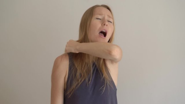 A young woman sneezes properly. She sneezes into her elbow