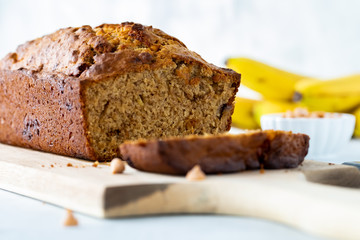A straight on close up view of a banana bread with one slice in front, resting on a wooden board.