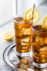 Very close up view of glasses of ice tea and lemon slices on a metal tray against a window sill.