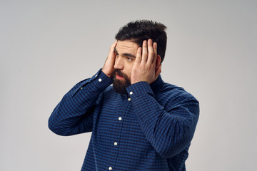 Side view of a man in a blue shirt touching his head with his hands