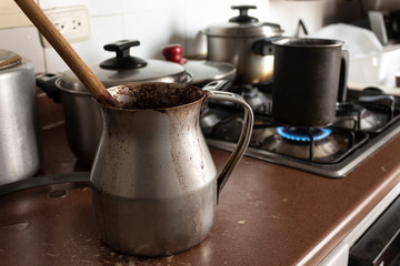 Old dirty cocoa cooking pot over kitchen furniture with gas stove on and others cooking pots at...