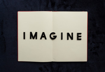 Close up to IMAGINE lettering over blank notebook at blue navy background.  Reading and study concept photography