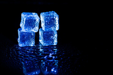 Blue ice cubes reflection on black table background.