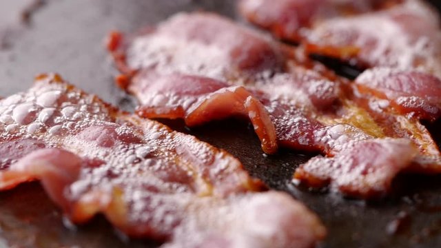 Camera follows cooking bacon on grill. Bacon dolly in slow motion.