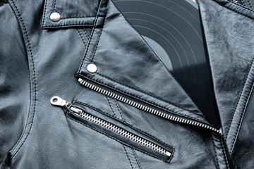 Closeup to a black leather biker jacket with LP vinyl disc. Music lover concept, retro photography.