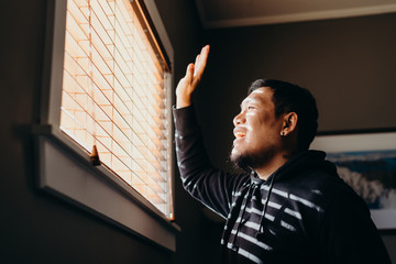 Asian man in isolation saying hi to people outside. Man forced to stay inside the house as a result of the restrictions caused by the Coronavirus outbreak.