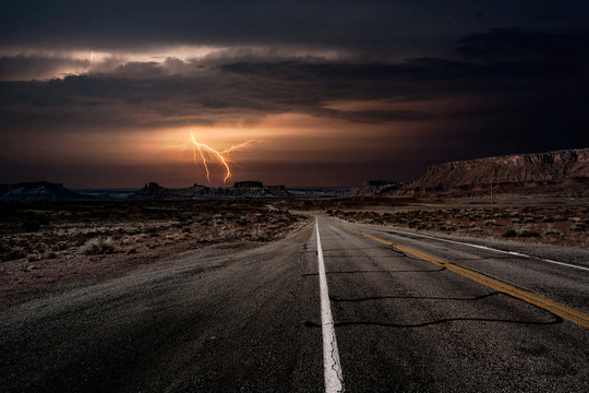 An empty highway leading to a lightning storm in the middle of the desolate desert near Moab, Utah, USA.