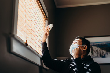 Asian man in isolation looking at medicine bottle. Man in medical mask forced to stay inside the...