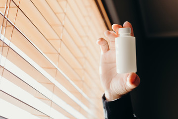 A man hand holding a medicine bottle against the  window.