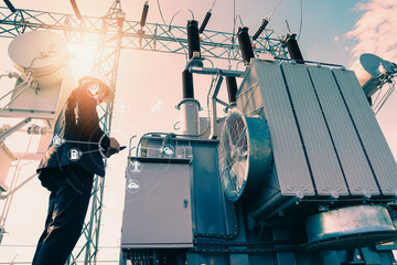Businessman wearing a black suit, standing looking at a large power transformer with orange...
