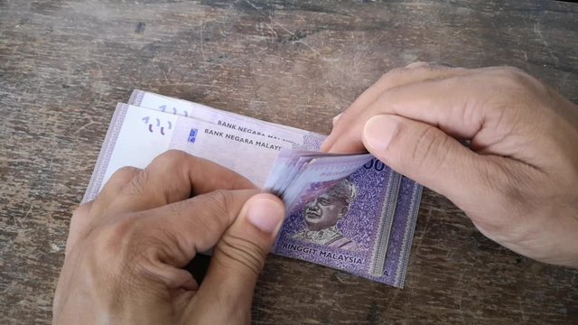 Hand calculates the banknote Ringgit Malaysia, value of the 100 on the wooden table. (selected focus)