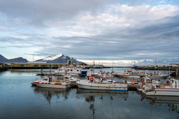 Fishing harbour in the city of HÃ¶fn in Iceland during sunset and blue hour. Fishing boats laying calm in the marina, reflections in the water infront and snow covered mountains in the background.