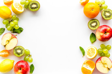 Fresh fruits background with citruses, apple, kiwi and grape on white table top-down frame copy space