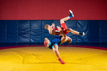 Two greco-roman  wrestlers in red and blue uniform wrestling  on a yellow wrestling carpet in the...