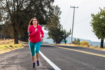 fitness, sport and healthy - smiling woman with earphones wearing armband for smartphone, jogging at summer on the highway and listening to music