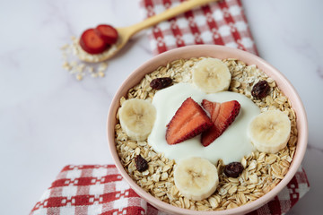 Healthy breakfast, bowl of oatmeal and yogurt with strawberry, banana and dried raisins