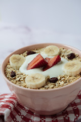 Healthy breakfast, bowl of oatmeal and yogurt with strawberry, banana and dried raisins