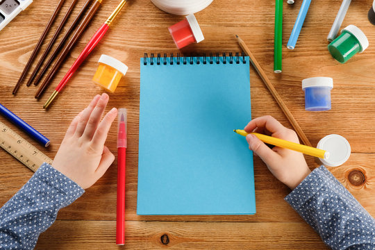 hand with a brush and paints. The child draws with paints and felt-tip pens in a notebook.