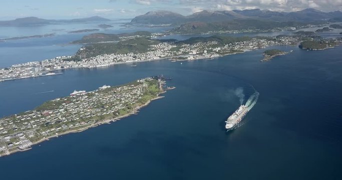 Cinematic and high altitude aerial drone footage of a luxurious cruise ship sailing in a fjord next to Alesund, the most beautiful town in Norway.