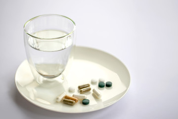 Fototapeta na wymiar Glass of water and pills on a plate isolated on white. Medicine and health concept.