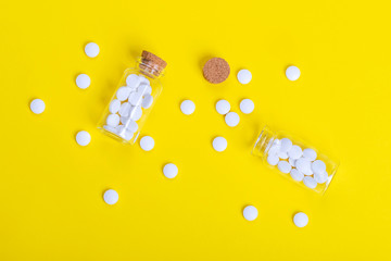 White and green tablets and bottles scattered on yellow background, top view, medicine concept
