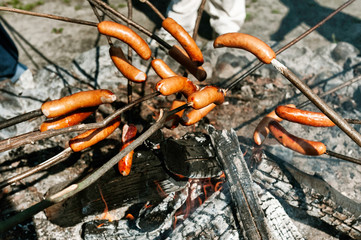 Sausages baked on a campfire in the forest. Making sausages over open camp fire. Grilling food over flames.