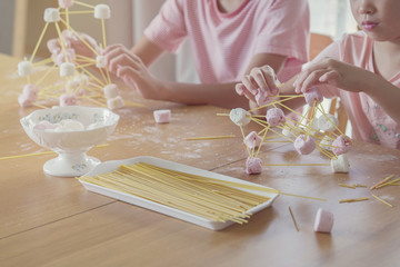 Mixed race young Asian children building tower with spaghetti and marshmallow learning remotely at...