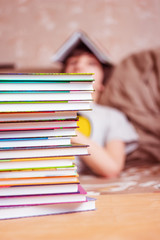 A stack of books against the backdrop of a teenager in defocus; the difficulties of home distance learning