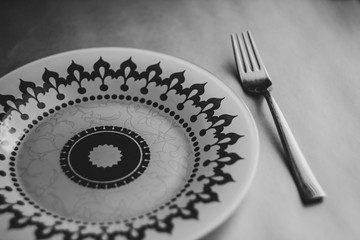 Cutlery on a gray table next to a striped napkin, glass plate with ornament, bnw 