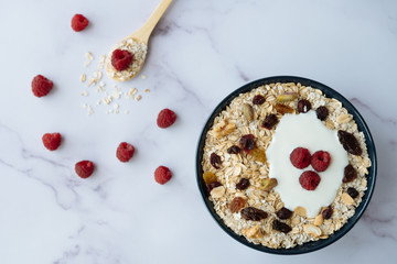 Healthy breakfast, bowl of oatmeal and yogurt with raspberry, nuts and dried raisins