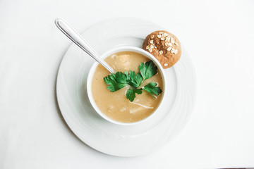 Puree soup with herbs and bread.White plate on the white minimalistic background.Top view