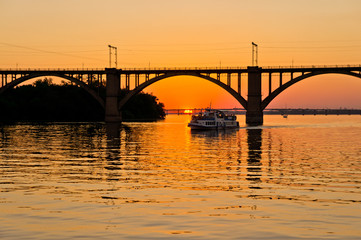 Fototapeta na wymiar A bridge on a river lit by the sun at sunset. Evening river landscape.