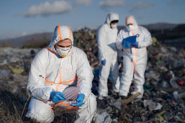 Group of activists with protective masks on landfill, environmental pollution concept.