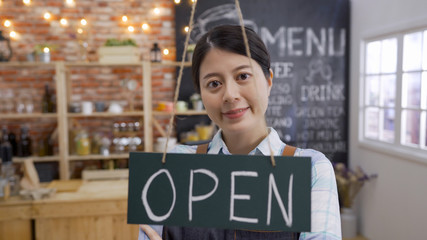 small business owner asian woman smiling and standing with crossed arms in cafe bar. beautiful waitress in entrance of coffee shop showing open sign door plate welcome face camera confident looking