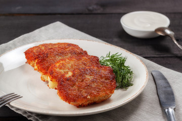 Potato pancakes with sour cream and dill on a wooden table