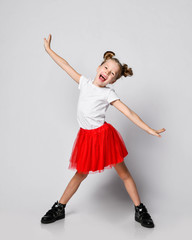 Singing laughing kid girl in fatin skirt and t-shirt stands holding her hands diagonal spread on white