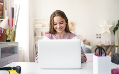 Young female student sitting at the table, using laptop in quarantine.