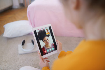 Unrecognizable young girl with tablet sitting at home, making video call.