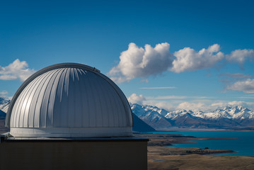 Obraz premium Bird’s eye view from Mt St John Observatory, with a view of the observatory dome, grassy hill overlooking a lake below with snow capped mountains in the background in Tekapo in New Zealand South Islan
