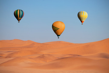 Fototapeta na wymiar Colored hot air balloons flying over the sand dunes at sunset