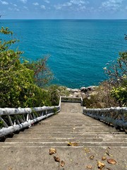 white staircase on the observation deck leading to the sea against a blue sky with white clouds and green trees under the sun in the tropics