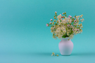 beautiful bouquet of wild flowers chamomile and clematis in a white jug on a blue green background closeup with a copy space