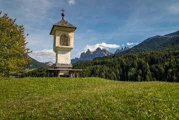 A beautiful church chapel with surrounding forest and countryside and The Dolomites Geisler Odle...