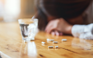 Closeup image of a sick woman sleep on table with white pills and a glass of water