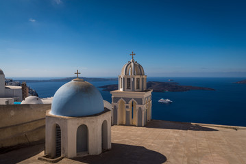 Fototapeta na wymiar Overlooking the beautiful blue Caldera ocean with the famous blue dome churches of Oia in the foreground in Santorini, Greece