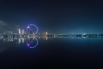 Panoramic shot from the bay of Singapore skyline at night with reflections of the city buildings and architecture in the background