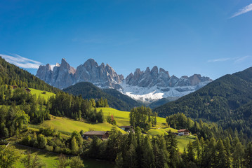 A scenic view overlooking a beautiful valley with surrounding forest and countryside and The Dolomites Geisler Odle mountain peaks in the background. Located in San Pietro, South Tyrol, Italy